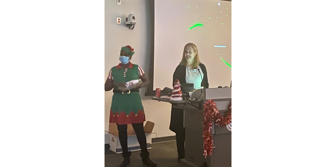Nancy Freitag and Arletta in an elf's costume standing at the podium
